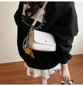 Gros plan du sac à bandoulière en cuir blanc avec boucle circulaire et breloque élégante