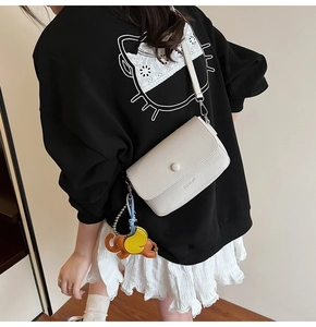 Detail of white lychee texture leather crossbody bag featuring elephant leather charm
