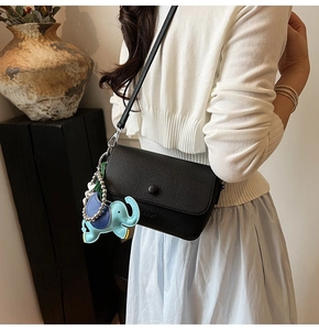 Detail view of black lychee grain crossbody bag with blue elephant charm on a model