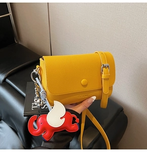 Close-up of yellow pebbled leather shoulder bag with elephant charm and silver buckle