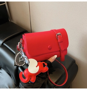 Detail of red pebbled leather shoulder bag with a flying elephant charm and logo