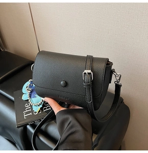 Detail of black lychee grain leather crossbody bag with silver hardware and blue flower charm