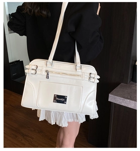 Detail of cream white tote bag with metal buckle straps and decorative brand logo plate