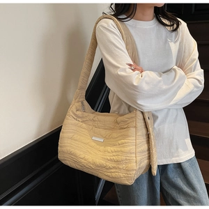 Detail of beige quilted shoulder bag with wavy stitching and wide strap on model