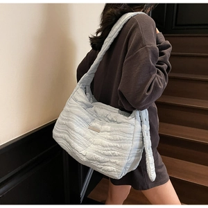 Detail of light blue quilted cloud tote bag with wavy stitching and metal logo plate