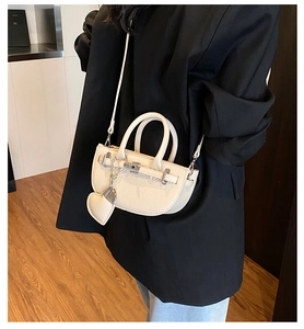 Detail of cream saddle bag with lychee grain leather, metal buckle, and heart charm