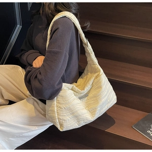 Detailed texture of off-white quilted tote bag with wavy fabric and metal plaque