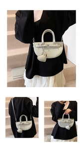 Detail view of cream lychee leather saddle bag with metal turn-lock and heart charm