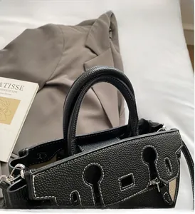 Detail of black pebbled leather handbag with contrast stitching and sturdy top handles