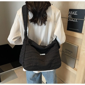 Detail of a large black quilted tote bag with wavy stitching shown on a model