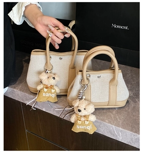 Detail of canvas bucket bags with leather trim and cute teddy bear charm on marble surface