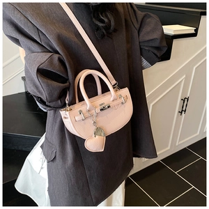Pink lychee texture crescent bag with heart charm shown on model in grey suit