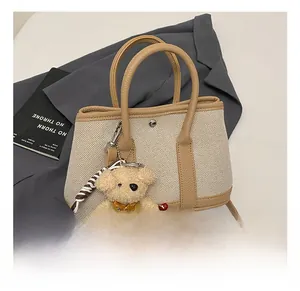 Detail view of canvas and leather bucket bag with a cute bear charm and dual handles