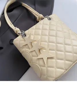 Détail d'un sac cabas matelassé crème avec breloques étoiles et finitions métalliques