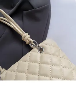 Détail de l'anneau argenté et bandoulière nouée sur sac seau matelassé en similicuir crème