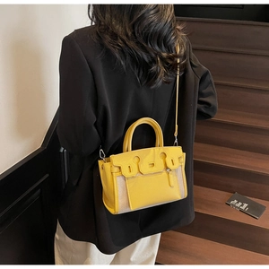 Detail view of yellow leather and canvas Kelly bag worn by a model on stairs