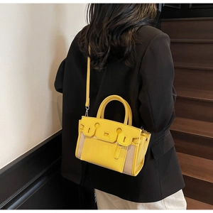 Detail of yellow lychee leather and beige canvas bucket bag with gold metal buckle