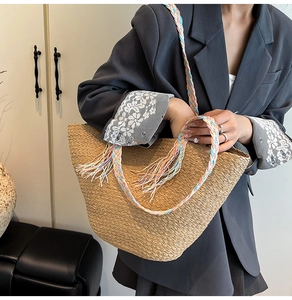 Dettaglio della borsa in paglia intrecciata a mano con manici colorati e nappe su modella