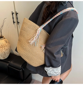 Dettaglio di una borsa tote in paglia intrecciata con tracolla colorata e nappe