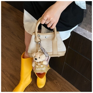 Close-up of canvas bucket bag with khaki leather trim and a cute plush bear charm