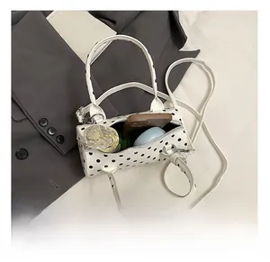 Internal capacity of polka dot cylinder bag showing phone, perfume and powder case