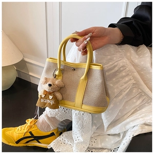 Detail of canvas bucket bag with yellow leather trim and a cute bear pendant decoration
