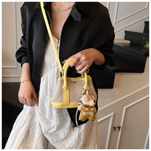 Detail of mini bucket bag showing yellow leather trim, canvas texture and bear charm