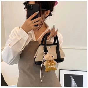 Detail of beige canvas and black leather bucket bag with a cute plush bear charm