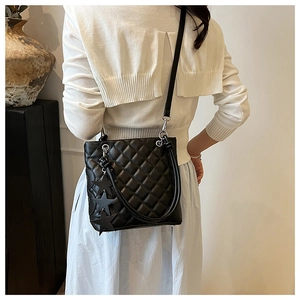 Détail d'un sac seau noir matelassé avec breloques étoiles porté par un mannequin