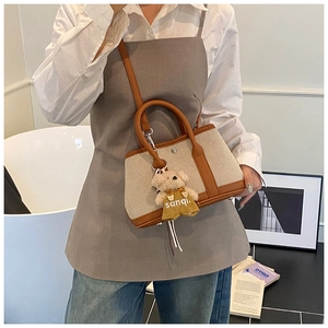 Detail of canvas tote with brown leather trim and cute plush bear charm accessory
