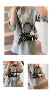 Detail view of black polka dot cylinder bag with lace bow and pearl charm accents