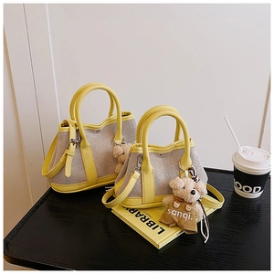 Detail of canvas bucket bags with yellow leather trim and a cute plush bear charm accessory