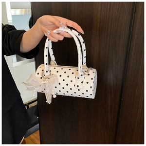 Close-up of white polka dot barrel bag with lace bow and pearl charm detail