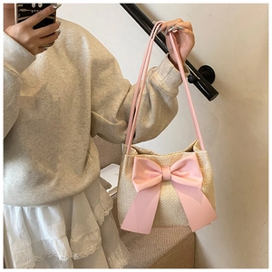 Sac seau en paille avec nœud en satin rose et bandoulière sur un mannequin
