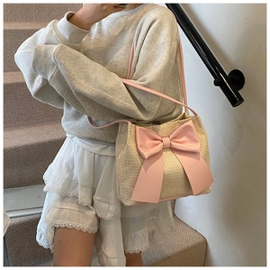 Détail du sac seau tissé beige avec un grand nœud rose décoratif sur escalier