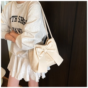 Détail de texture d'un sac bandoulière tissé avec un grand nœud en satin de couleur crème