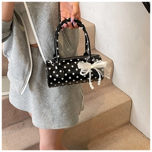 Close-up of black and white polka dot cylindrical handbag with lace bow and pearl charm