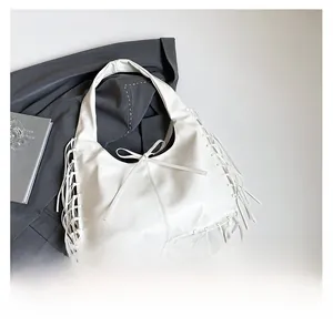 Détail d'un sac hobo blanc avec de longues franges et un nœud posé sur un blazer
