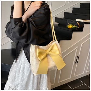 Détail d'un sac à bandoulière tressé beige avec un nœud en cuir jaune sur le bras