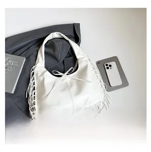 Détail du sac hobo blanc à franges sur un fond de blazer gris élégant et sobre