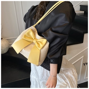Détail d'un sac seau en paille crème avec un grand nœud jaune et une bandoulière