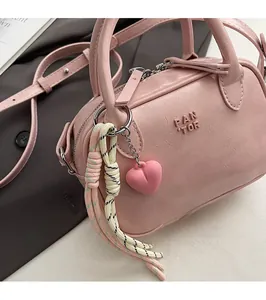 Détail du sac Boston rose montrant les poignées, le zip et l'accessoire pendentif coeur