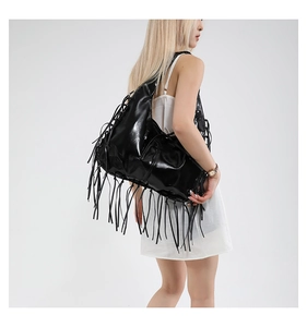 Detailed view of large black patent leather tote bag with long fringe tassels on model