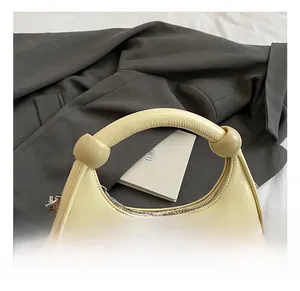 Detail of cream crescent bag featuring ball-knotted handle and silver zipper on suit jacket