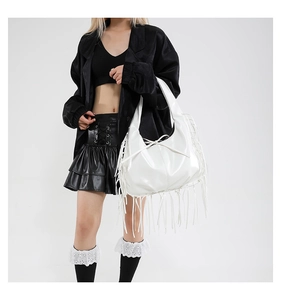Detail of white glossy fringe tote bag with tassels and bow on a dark-outfit model