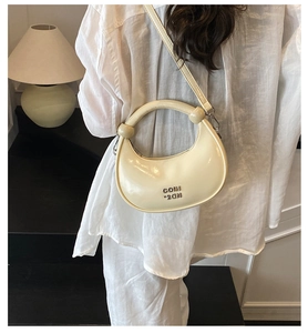 Detail of cream crescent bag featuring glossy patent leather and metallic logo lettering
