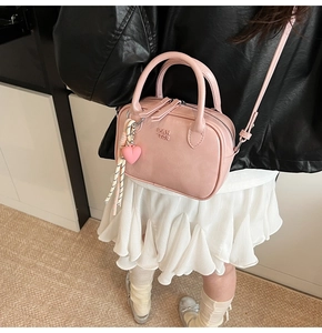 Détail du sac à main en cuir rose avec breloque cœur et logo PAN TOR embossé