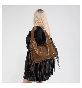 Model wearing dark brown glossy shoulder bag with long fringe and bow details