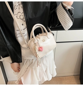 Détail d'un sac bandoulière blanc crème en cuir avec breloque cœur et logo sur le côté