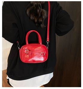 Red faux leather bowling bag with bow detail and silver buckles worn on a hoodie